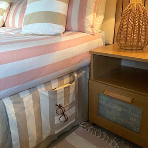 A close-up of a beige and white striped fabric bed mattress storage pocket holding a pair of glasses and a book