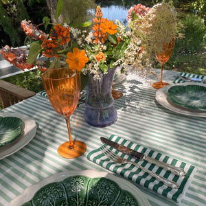 An outdoor dining table styled with a celadon green and white striped tablecloth, shamrock green stripe napkins