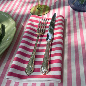 A magenta pink and white striped cotton napkin on a candy pink striped tablecloth
