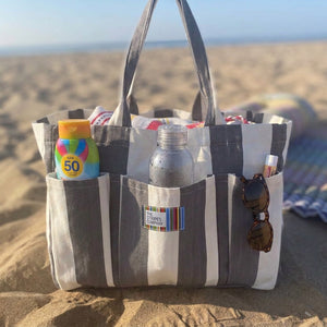 A striped beach tote bag with sunscreen bottle, water bottle, sunglasses, and other beach items in its pockets