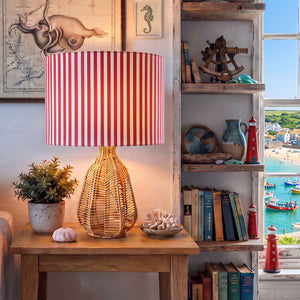 A coastal-themed table lamp with a red and white striped fabric drum shade and a woven rattan base, styled with nautical decor.