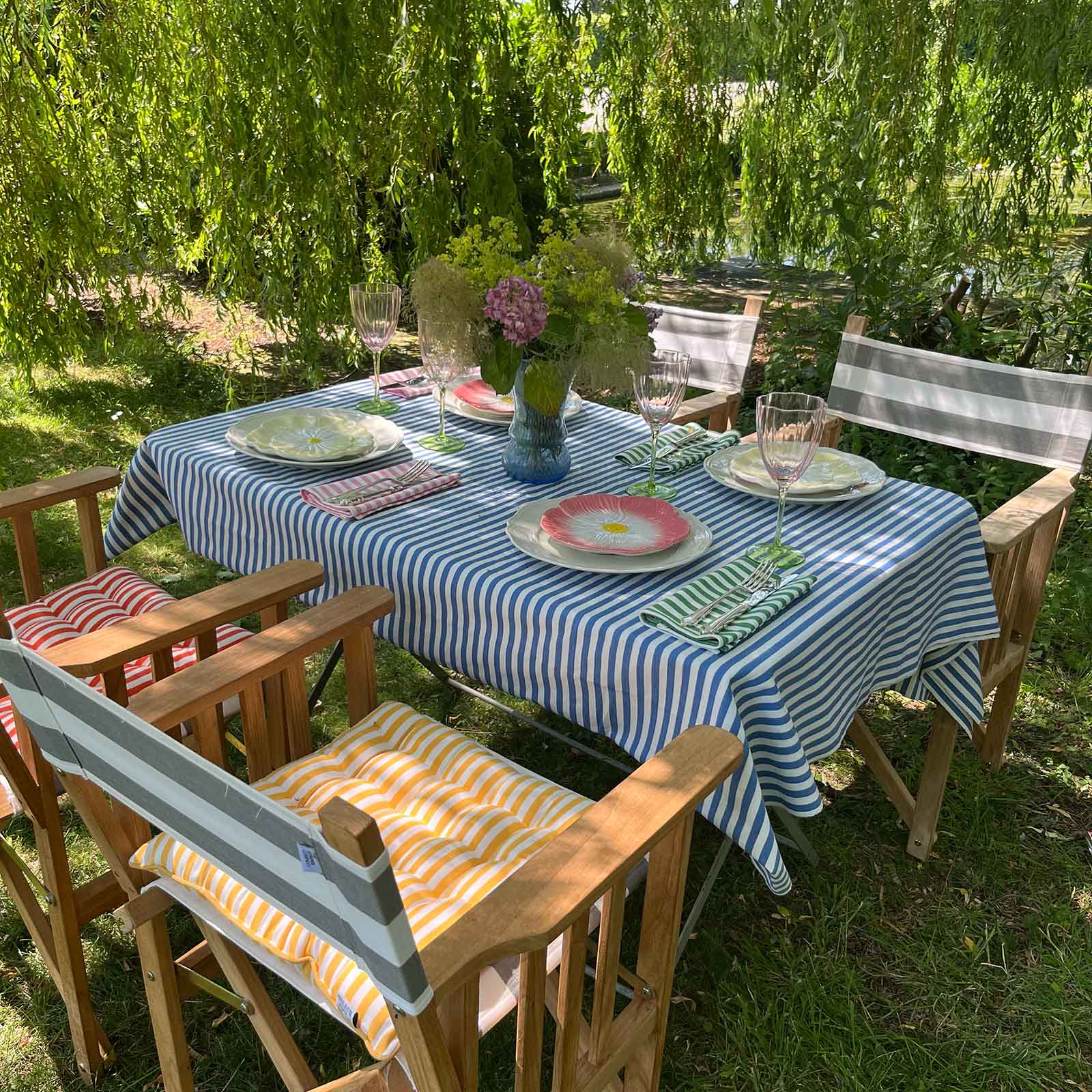 Rectangular blue and white striped tablecloth and striped napkins on table surrounded by directors chairs with striped cushions.