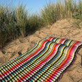 Colourful striped beach mattress on a sandy beach with grasses.