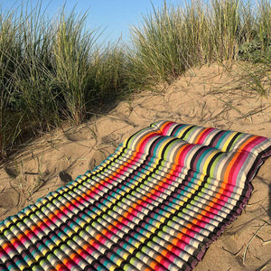 Colourful striped beach mattress on a sandy beach with grasses.