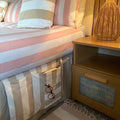 A close-up of a beige and white striped fabric bed mattress storage pocket holding a pair of glasses and a book
