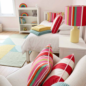 A styled children's bedroom featuring  colourful striped cushions and lampshade in pink red and white stripes with hints of yellow and green