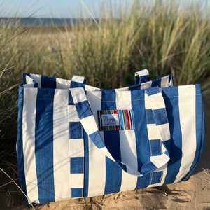 the stripes company Blue and white striped beach bag on a sandy beach.