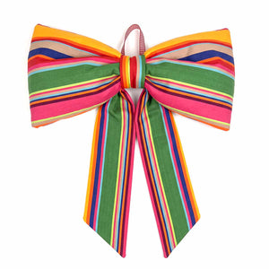 A large fabric bow with a vibrant multicolour striped pattern, featuring green, pink, orange, yellow, blue, and red stripes, set against a plain white background.