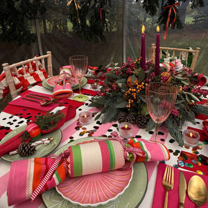 A festive Christmas table setting with pink and red striped reusable crackers and napkins