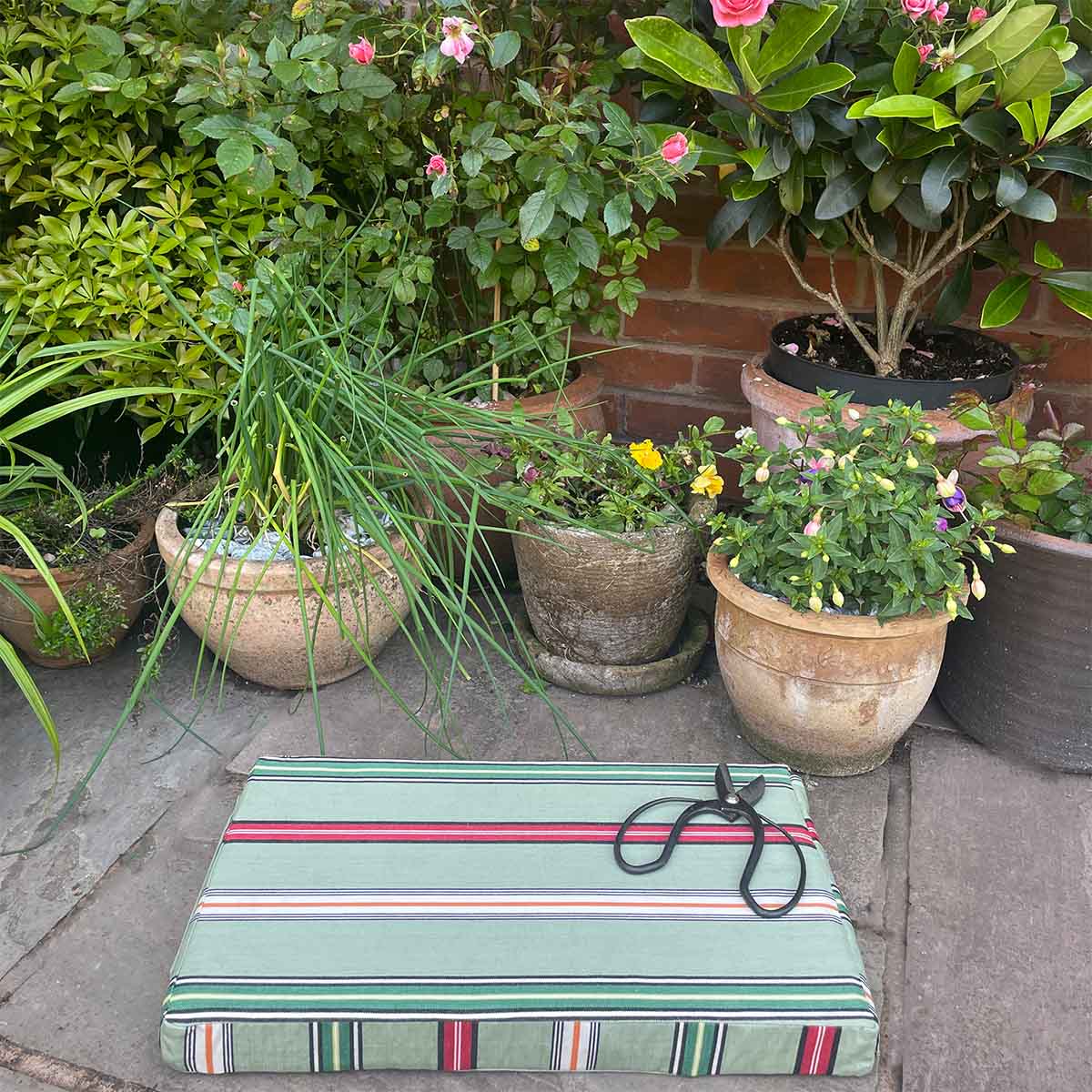 Striped kneeling pad for gardeners on a stone surface with potted plants in the background