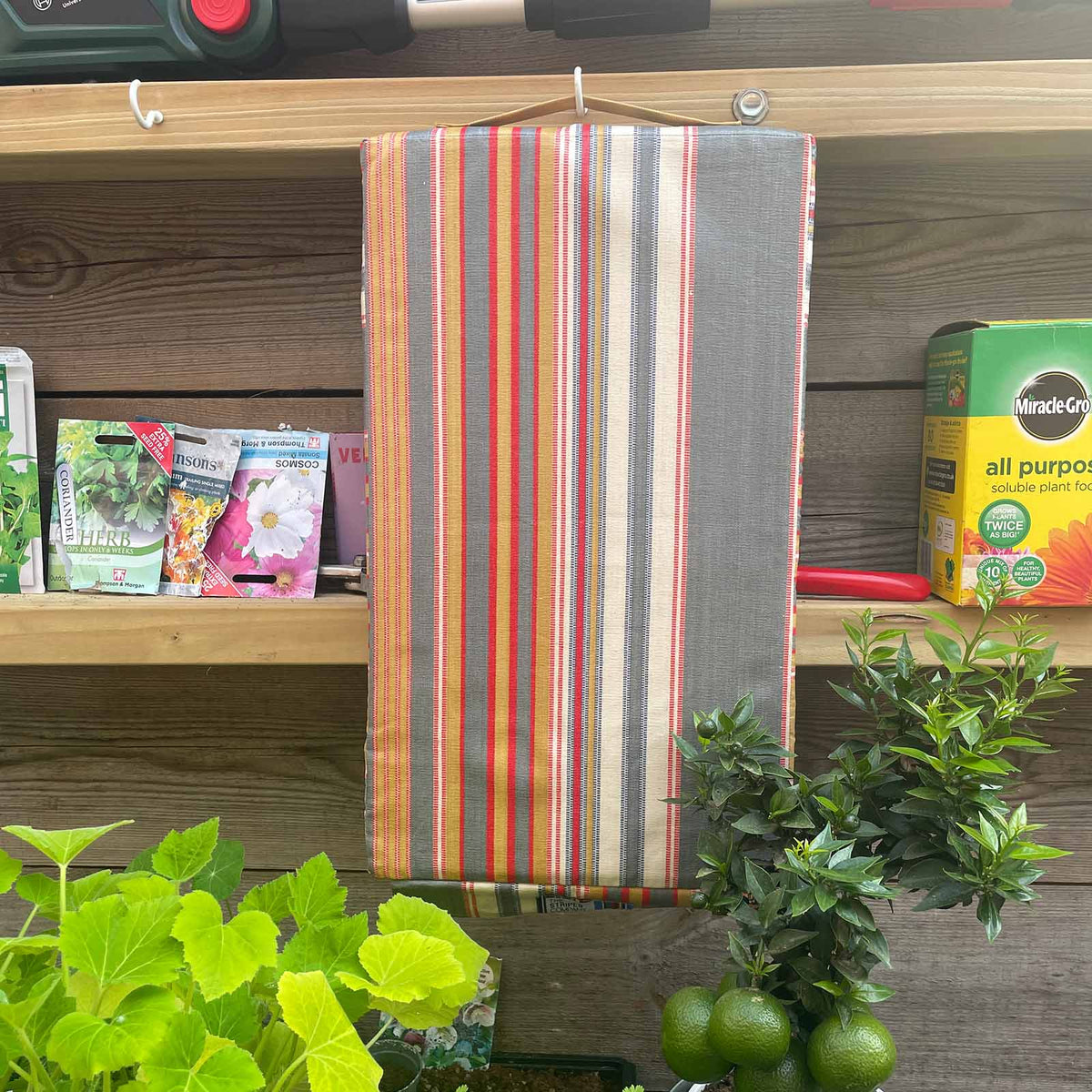 kneeling pad hanging on a wooden shelf with gardening supplies and plants.