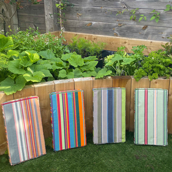 Four colourful striped garden kneeler pads against a wooden raised garden bed with plants.
