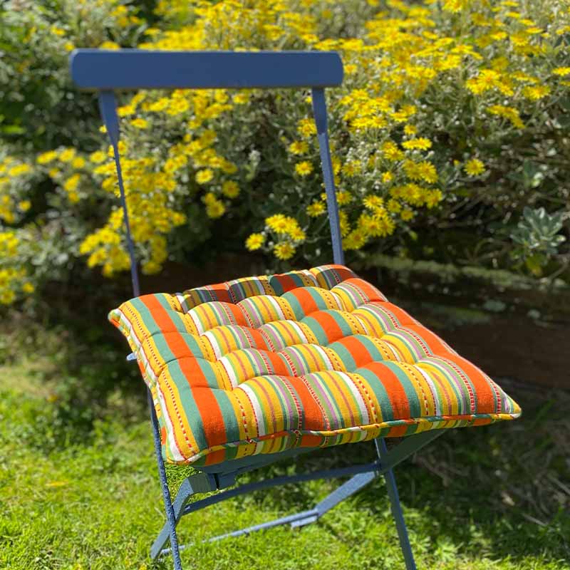 colourful striped cushion on a chair in a garden with yellow flowers.