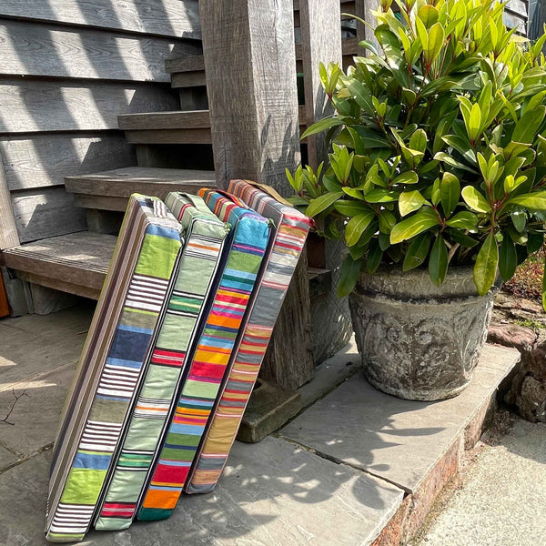Colourful striped gardening kneeler pads leaning against a wooden wall with a plant in the background.