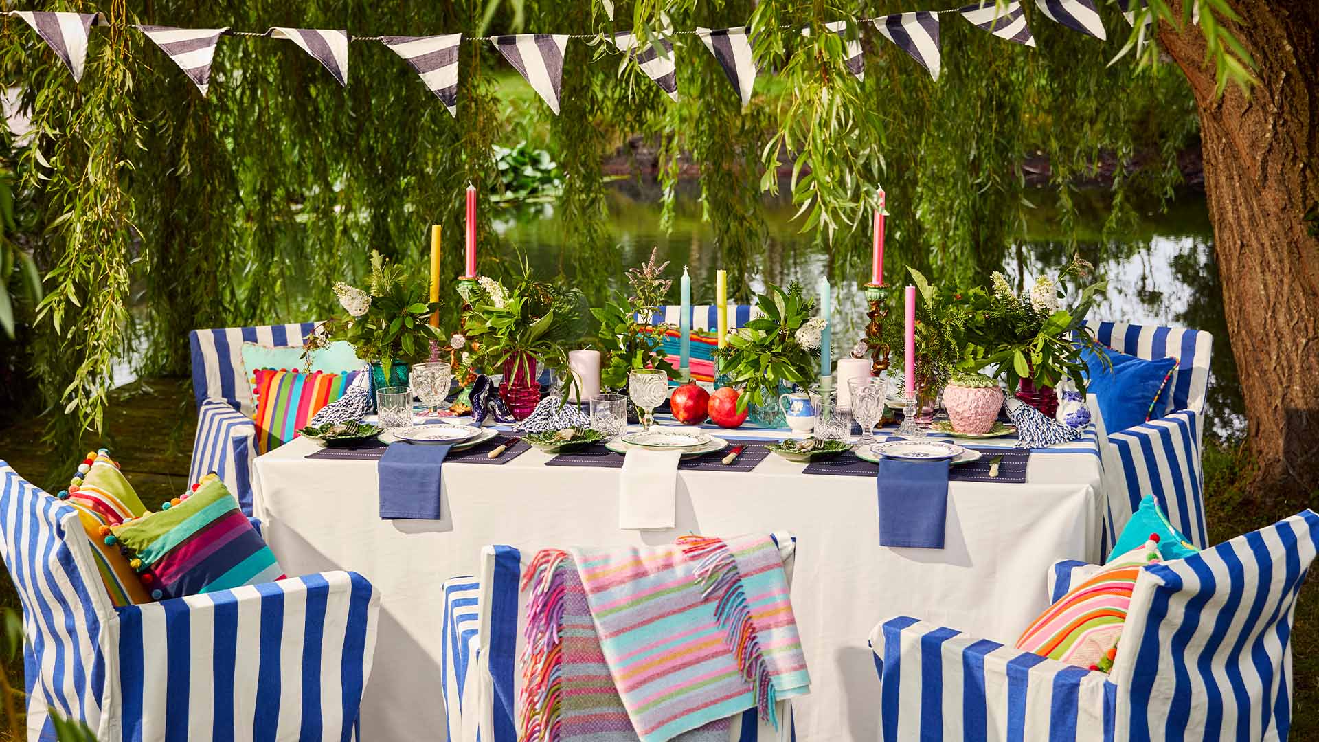 Outdoor dining setup with striped chairs, colourful table settings, and striped bunting.