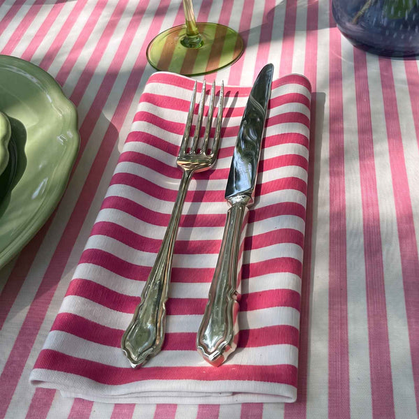 A magenta pink and white striped cotton napkin on a candy pink striped tablecloth