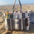 A striped beach tote bag with sunscreen bottle, water bottle, sunglasses, and other beach items in its pockets 