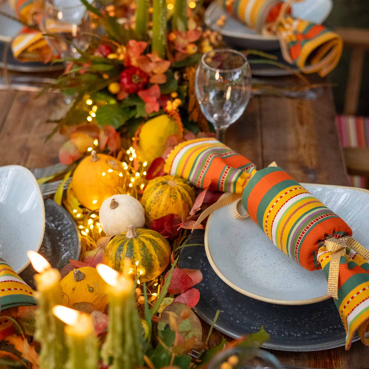 autumn-themed table with reusable striped fabric cracker with orange, green, yellow and white stripes, styled with small pumpkins