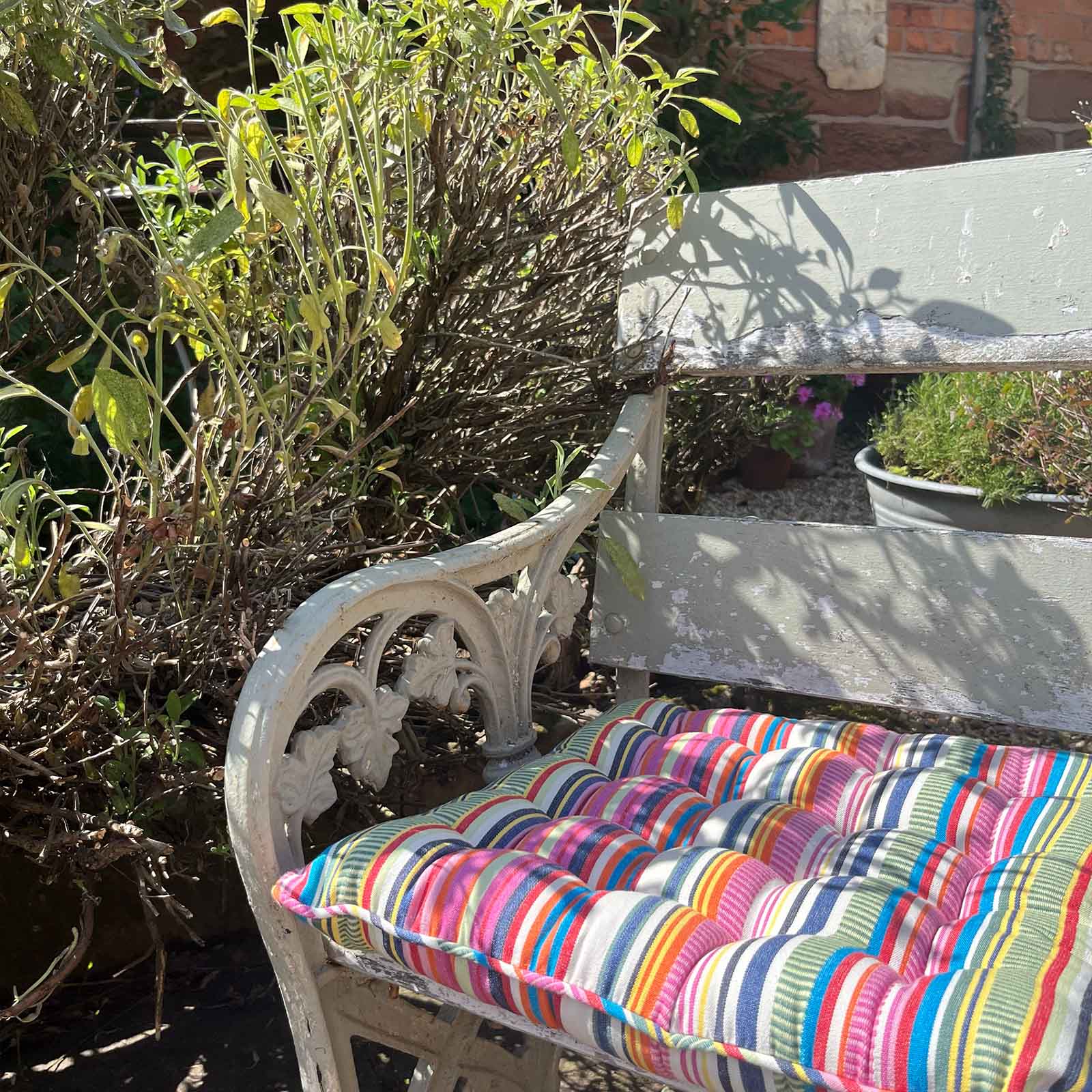 colourful striped cushion on a white wrought-iron garden bench