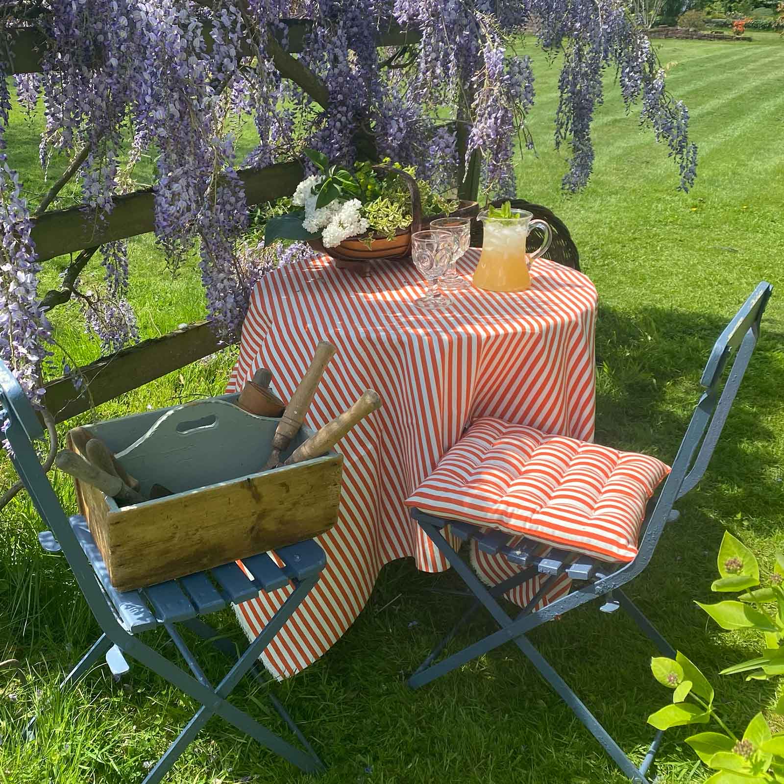 orange-and-white stripe tablecloth-covered table, chairs with seat pad, and wisteria in a garden.