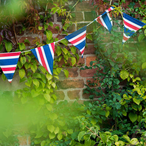 British flag bunting hanging against a brick wall with greenery