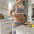 colourful striped apron with pockets in soft blues, pinks, lime green stripes in a bright, modern kitchen with white cabinets and marble countertops.
