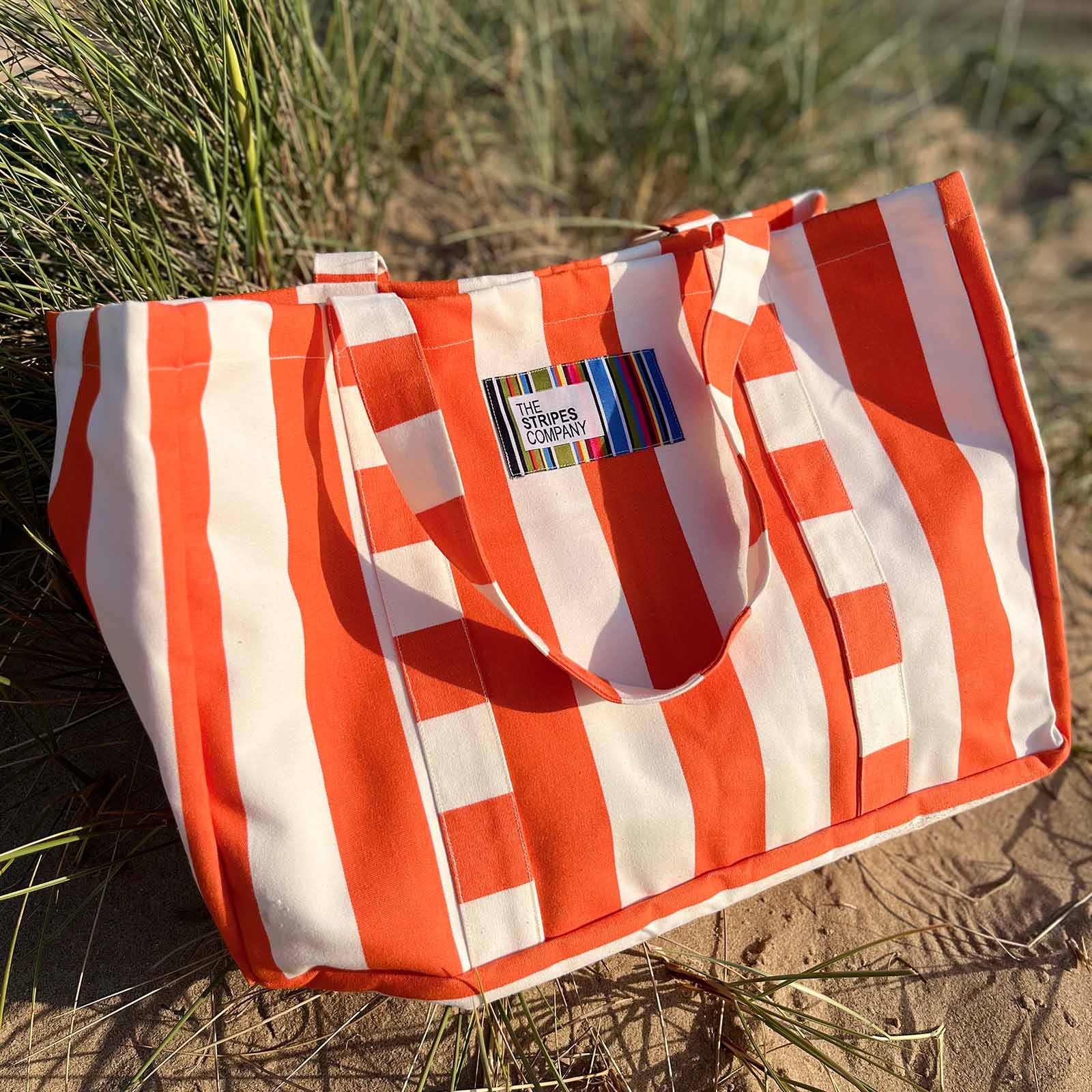 orange and white striped bag - the stripes company brand on a sandy beach