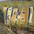 Yellow, blue, and white striped bag on a beach.