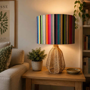 A table lamp with a colourful vertically striped fabric drum shade