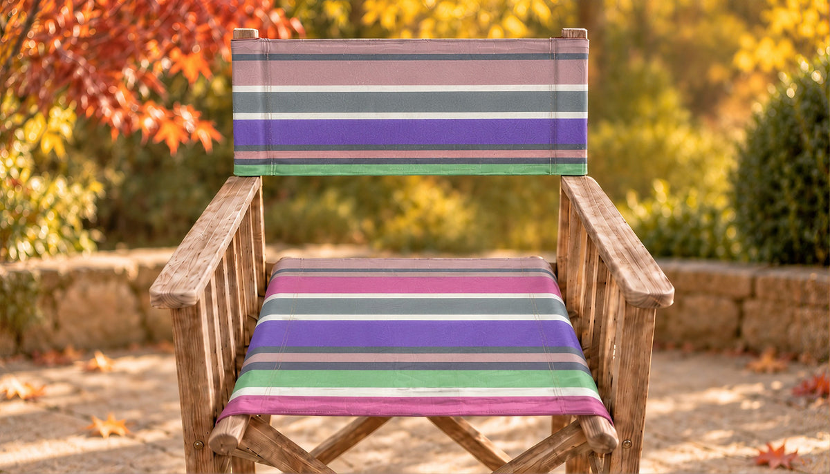 after recovering a wooden directors chair with a striped fabric seat and backrest in purple, green, gray, and pink, set against a blurred autumn garden background.