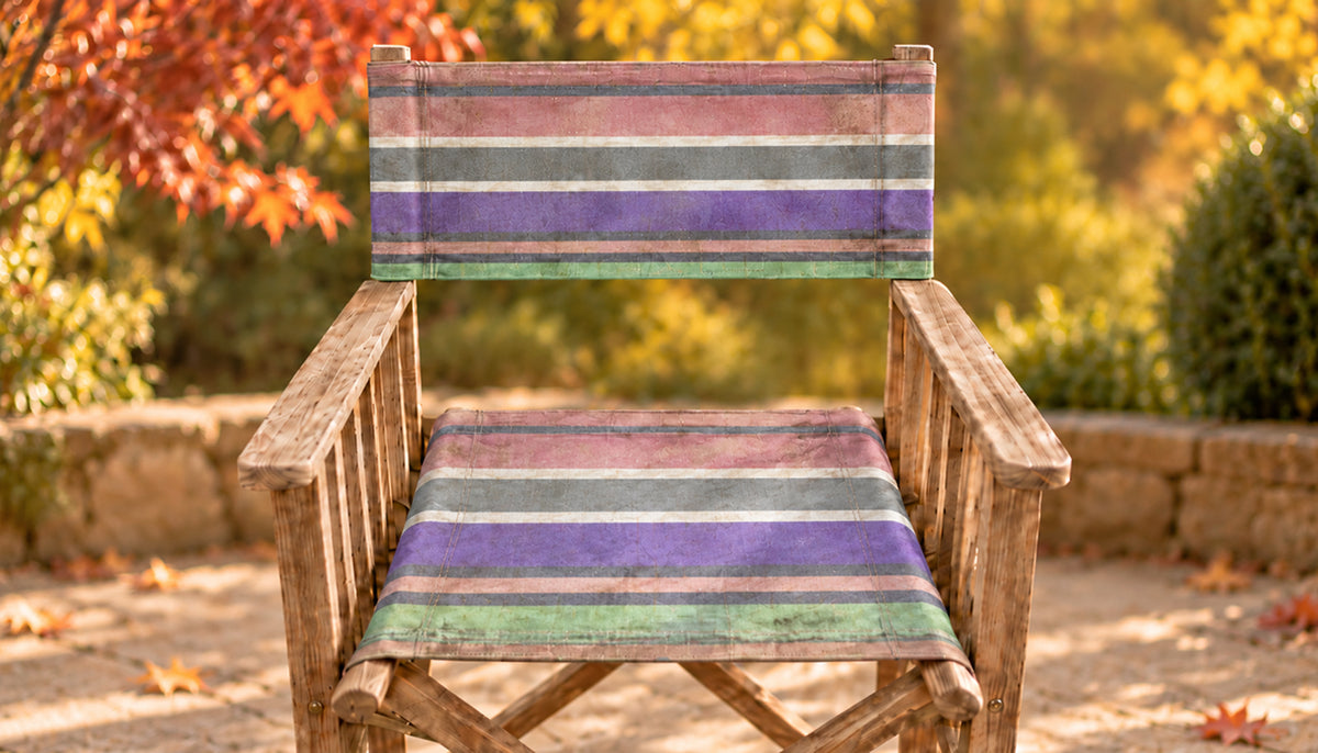 before recovering rustic wooden directors chair with a striped fabric seat and back in purple, green, and pink tones, set against a blurred autumn garden background.