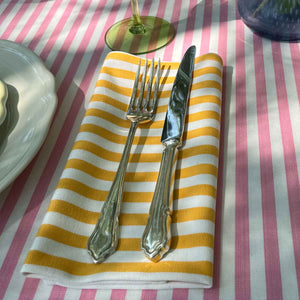 A folded striped napkin in yellow and white  stripes on a pink and white striped tablecloth